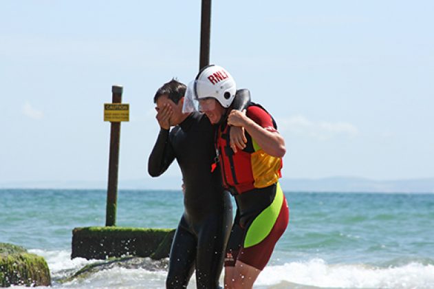 RNLI lifeguard helping ashore a casualty (putting arm around shoulder) during the One Big Rescue demonstration at Branksome Chine, Dorset.