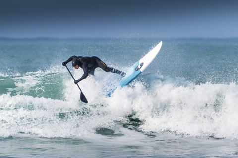 A paddle boarder riding a wave at Fistral in Newquay, Cornwall.